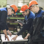 Men with drawings working in an old factory to install the equipment in protective helmets